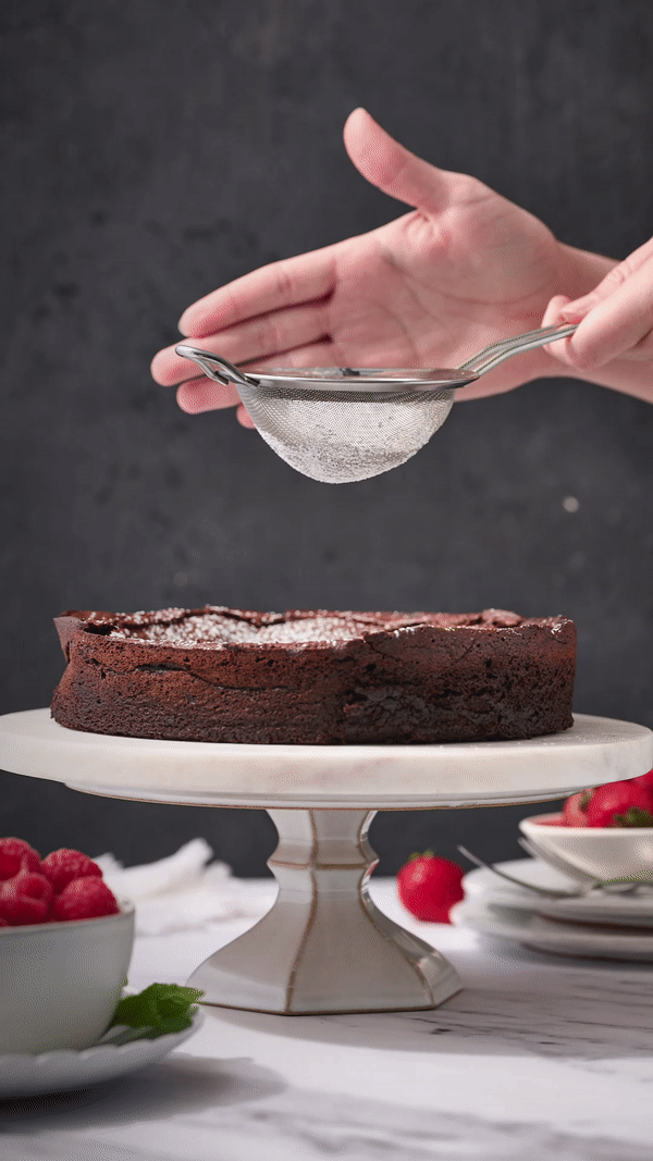 gif showing powdered sugar being sprinkled over the cooled flourless chocolate cake.