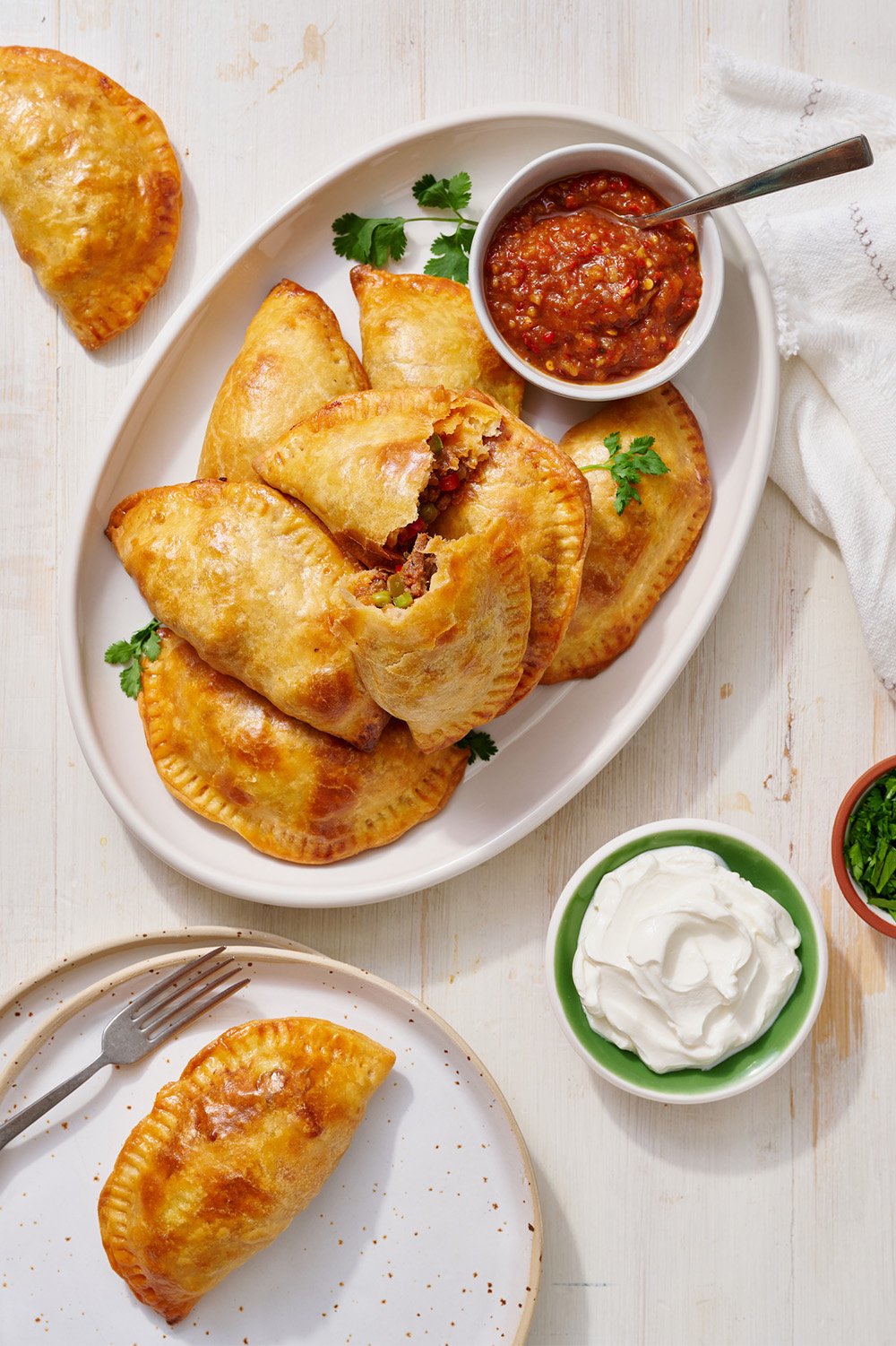 beef empanada on a plate with some salsa and sour cream for dipping.