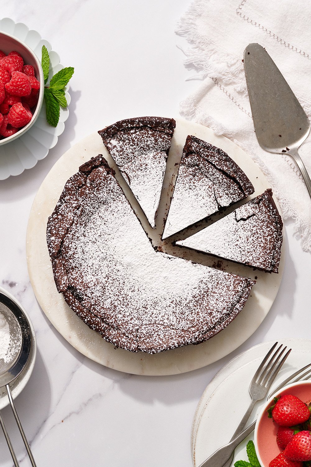 the whole flourless chocolate cake from above, o a white platter, with a few slices cut and ready to be served.