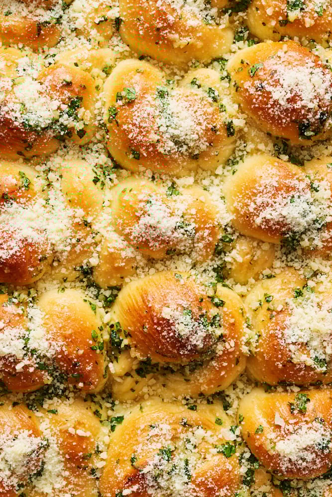 close shot of the garlic knots in their pan, covered in garlic butter, fresh parsley, and grated Parmesan. 