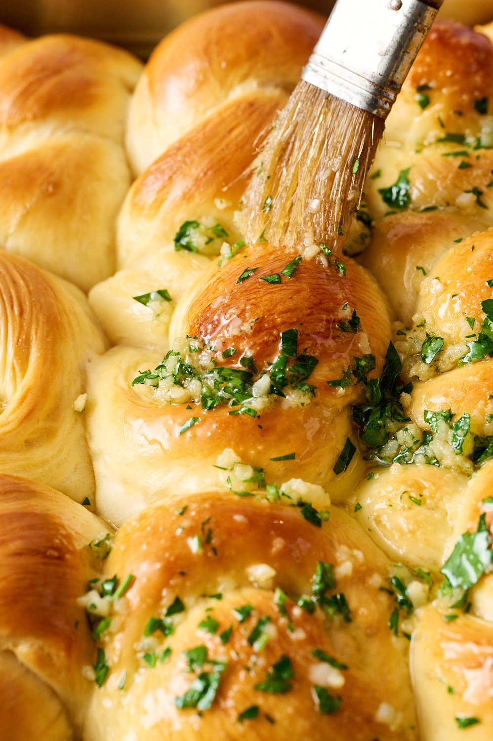 garlic butter being brushed on top of the warm rolls.