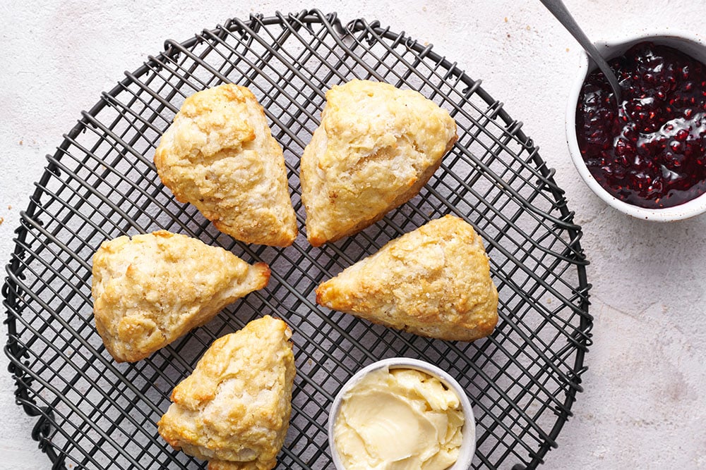 scones on a wire tray with small pots of butter and jam.