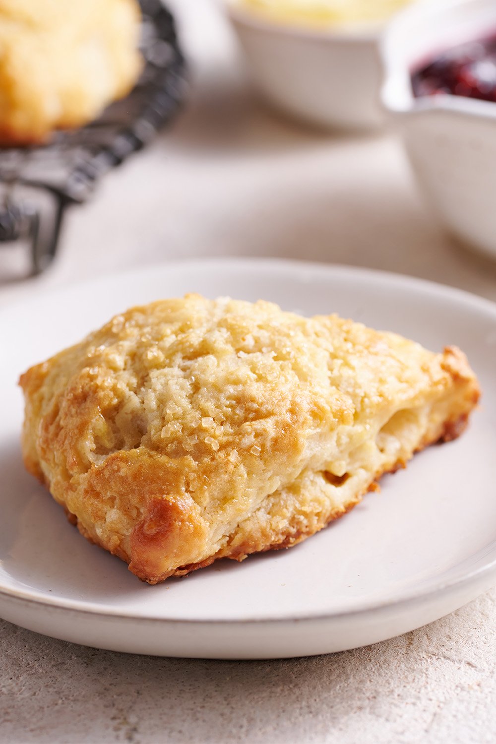 single scone sitting on a plate, with jam in the background, ready to serve.