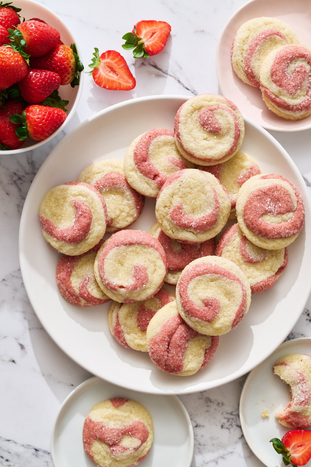 a white plate full of strawberry swirl sugar cookies, with some fresh strawberries nearby.