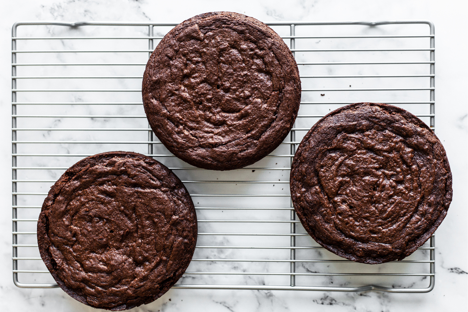 three layers of rich, fudgy brownie cake on a cooling rack on a marble countertop